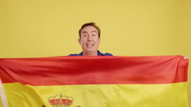 Улыбающийся Взрослый Мужчина Поднимает Испанский Флаг Студии Жёлтым Фоном — стоковое видео