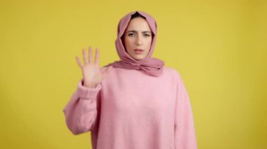 Muslim woman gesturing prohibition with hand in studio with yellow background