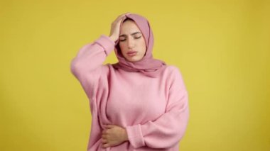 Muslim woman gesturing bodily discomfort and headache in studio with yellow background