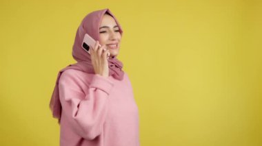 Happy muslim woman talking to the mobile phone in studio with yellow background