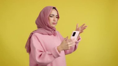 Stüdyoda sarı arka planda cep telefonu kullanan endişeli müslüman kadın.