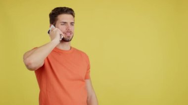 Angry caucasian man talking to the mobile in studio with yellow background