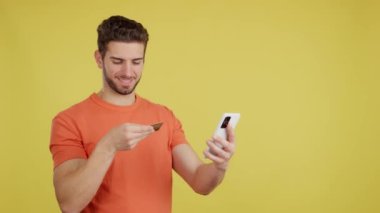Caucasian man using the mobile and card to shopping online in studio with yellow background