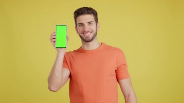 Stüdyoda sarı arka planda krom ekranlı cep telefonu tutan mutlu beyaz adam.
