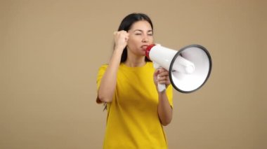 Upset caucasian woman yelling using a loudspeaker in studio with brown background