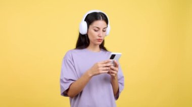 Caucasian woman listening to music and dancing in studio with yellow background