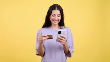Happy woman using the mobile and card to shopping online in studio with yellow background