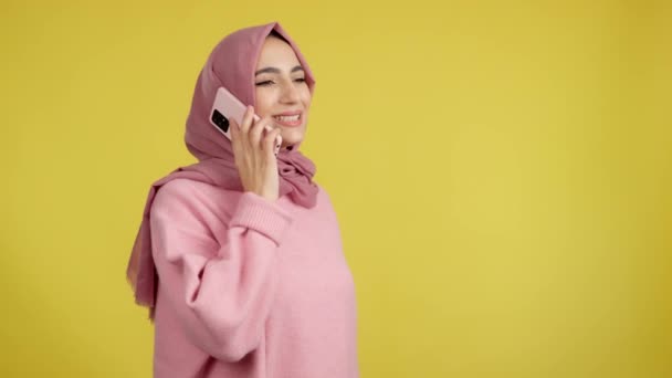 快乐的穆斯林女人在有黄色背景的工作室里与手机交谈 — 图库视频影像