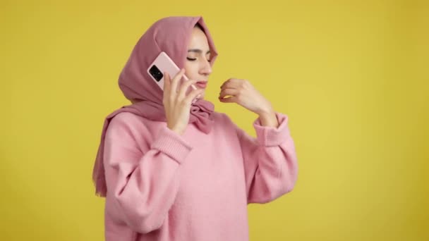 怒っているイスラム教徒の女性は黄色の背景を持つスタジオでモバイルと話して — ストック動画