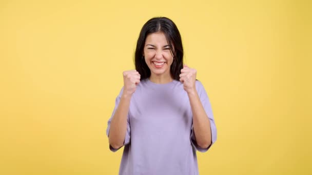 黄色の背景を持つスタジオで腕を上げながら幸せなヒスパニック系の女性のお祝い — ストック動画