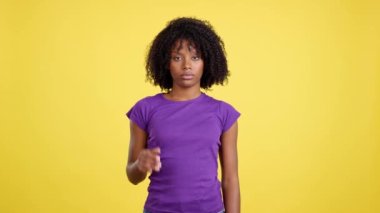 Woman with African hair gesturing rejection in studio with yellow background
