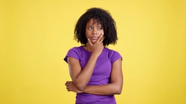 Woman with afro hair standing with thoughtful expression in studio with yellow background