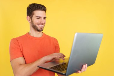 Caucasian man smiling while using a laptop in studio with yellow background