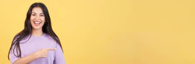 Happy woman pointing a blank space to the side in studio with yellow background