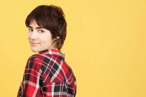 Androgynous person turning to smile at the camera in studio with yellow background