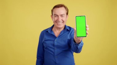 Chroma screen of the mobile held by a mature man in studio with yellow background