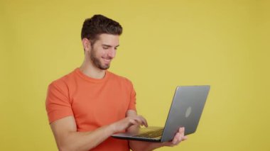 Caucasian man smiling while using a laptop in studio with yellow background