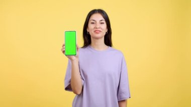 Happy woman holding a mobile with a chroma screen in studio with yellow background