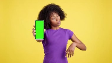 Stüdyoda sarı arka planda yeşil ekranlı cep telefonu olan afro bir kadının eli.