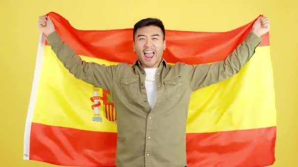 Chinese Man Smiling Raising Spanish National Flag Studio Yellow Background — Stockvideo