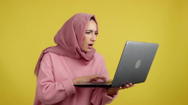驚くべきイスラム教徒の女性とともに頭スカーフ使用してノートパソコンでスタジオで黄色の背景 — ストック動画