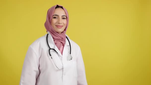 Szczęśliwa Kobieta Muzułmanin Lekarz Ramionami Skrzyżowane Patrząc Kamerę Studio Żółtym — Wideo stockowe