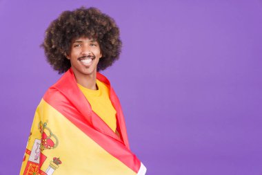 Afrikalı bir adam stüdyoda İspanyol bayrağıyla kameraya gülümsüyor.