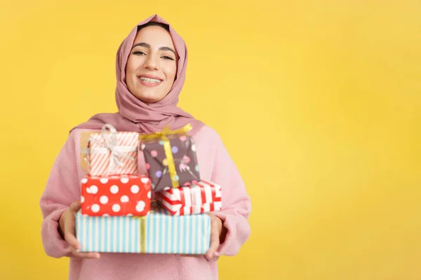 幸せなイスラム教徒女性とともにスカーフ保持多くの贈り物でスタジオで黄色の背景 — ストック写真