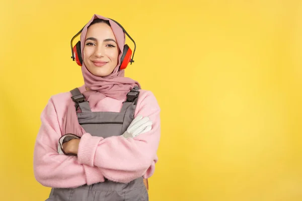 黄色の背景を持つスタジオでカメラを見て仕事の制服で優しいイスラム教徒の女性大工 — ストック写真