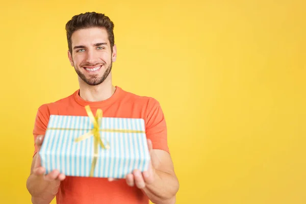 Kameraya bakan mutlu beyaz adam stüdyoda sarı arka planlı bir hediye veriyor.