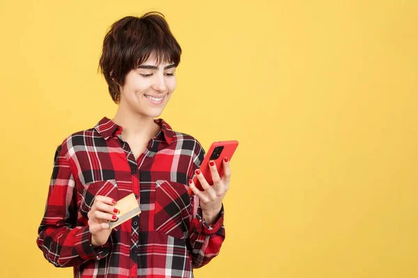 Androgynous person shopping online with a mobile in studio with yellow background