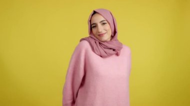 Stüdyoda sarı arka planda bir hediye verirken kameraya gülümseyen mutlu Müslüman kadın.
