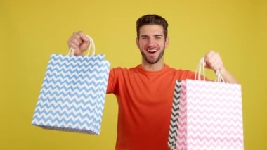Caucasian man raising many shopping bags while smiling in studio with yellow background