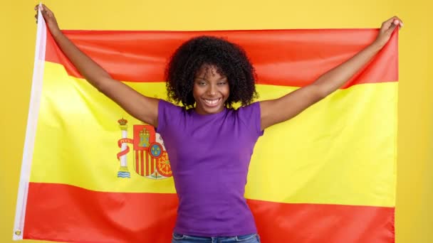 快乐的非洲女人笑着在有黄色背景的工作室升起西班牙国旗 — 图库视频影像