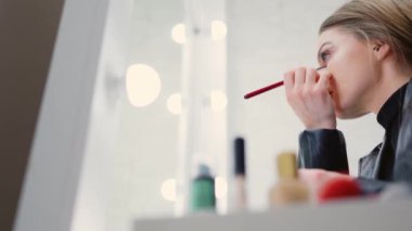 Sahne arkasındaki göz hizasına makyaj yapan bir kadının düşük açılı videosu.