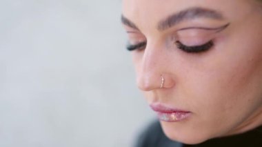 Bir kadının sahne arkasında fırçayla dudaklarına parlatıcı sürdüğü yavaş çekim videosu.