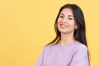 Stüdyoda sarı arka planda kameraya gülümseyen mutlu İspanyol kadın.