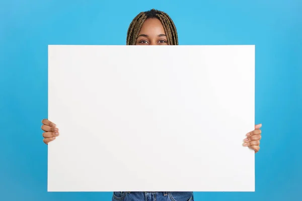Beyaz bir afiş tutan Afrikalı bir kadının mavi arka planlı stüdyo portresi.