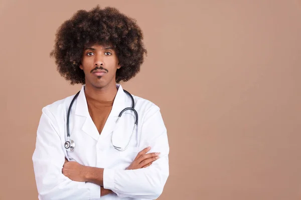 Serious african doctor with curly hair standing and looking at the camera with arms crossed in studio