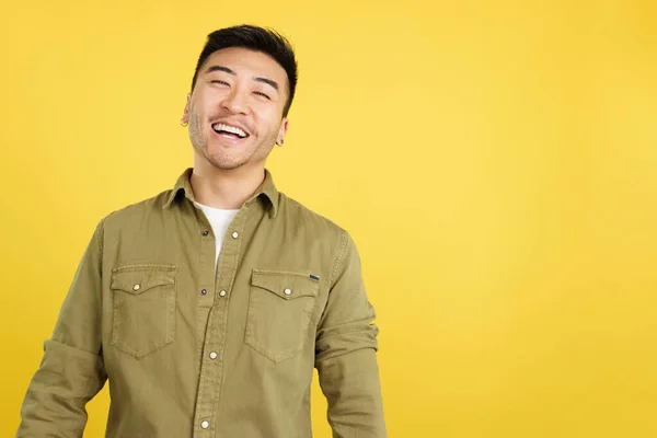 Chinese man laughing and looking at camera in studio with yellow background