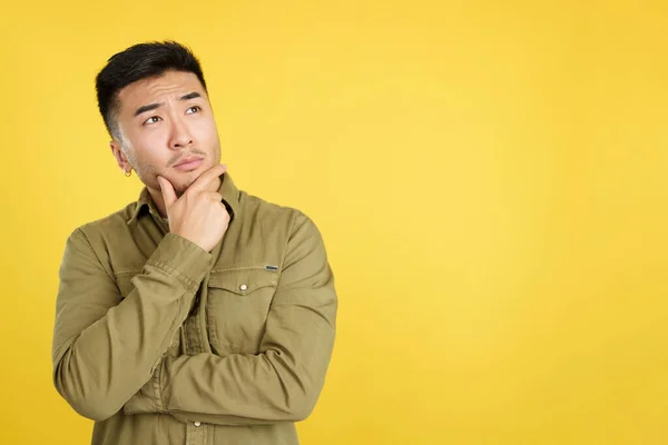 Chinese man with hand on face and thoughtful expression in studio with yellow background