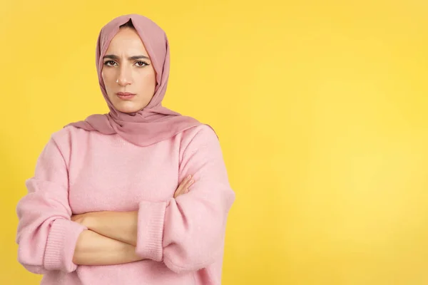 イスラム教徒の女性は黄色の背景とスタジオで怒っている式で腕を横断 — ストック写真