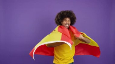 Afrikalı bir adam stüdyoda İspanyol bayrağıyla kameraya gülümsüyor.