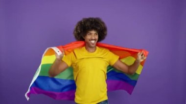 Happy african man smiling at camera wrapped with a lgbt flag in studio