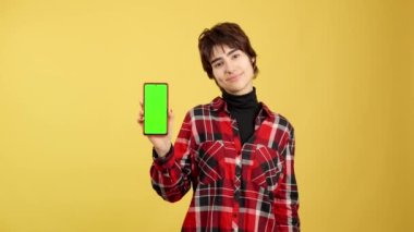 Androgynous sarı arkaplan ile yeşil mobil ekrana bakıyor