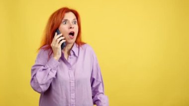 Stüdyoda sarı arka planda cep telefonuyla konuşan olgun kızıl saçlı kadın.