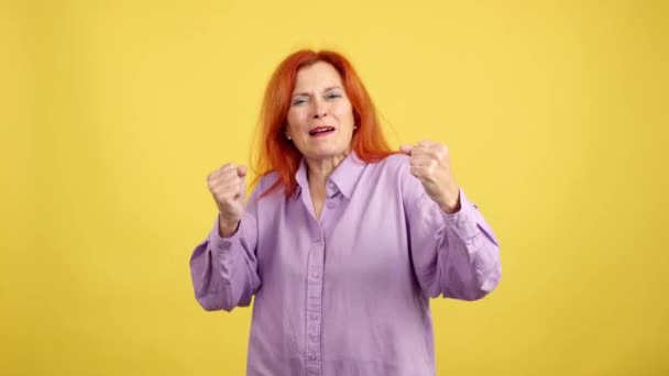 黄色の背景を持つスタジオで腕を上げながら色素の赤毛のお祝いと幸せな成熟した女性 — ストック動画