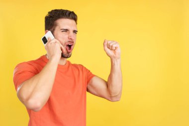 Stüdyoda sarı arka planda cep telefonuyla kutlama yapan mutlu beyaz adam.