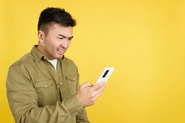 中国男人在黄色背景的工作室里用手机表示担忧 — 图库照片