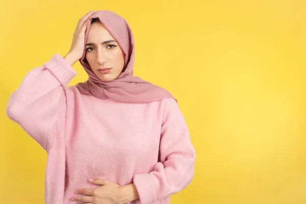 イスラム教徒の女性ジェスチャー体不快感と頭痛でスタジオで黄色の背景 — ストック写真